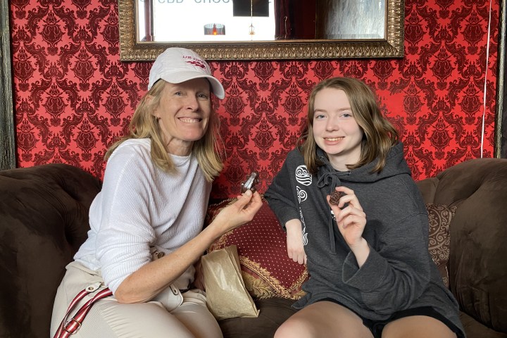 Two people sitting on a couch with red patterned wallpaper, holding chocolate.