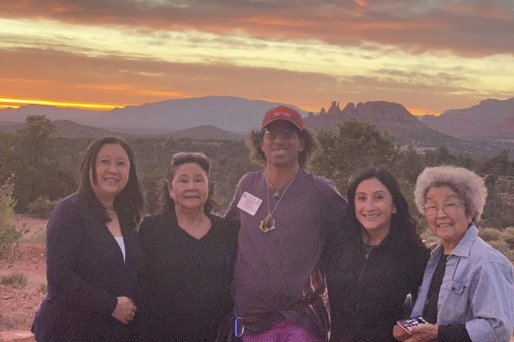 Five people posing outdoors at sunset with a colorful sky and mountains in the background.