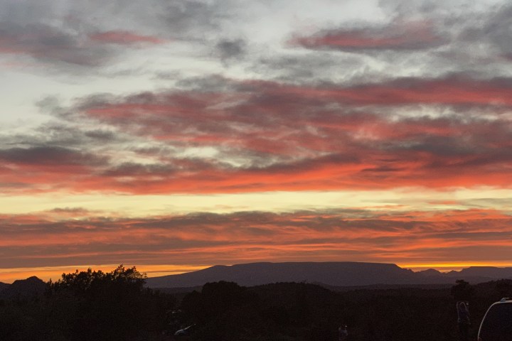 Vivid sunset with red, orange clouds over dark landscape, silhouette of hills and trees.