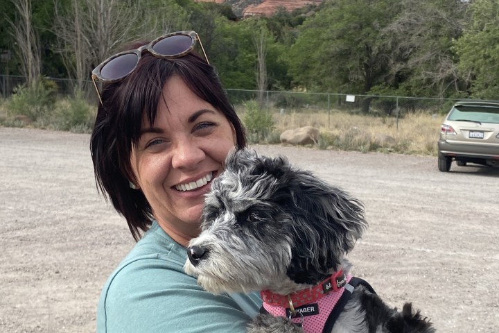 Woman smiling and holding a small black and white dog with mountains in the background.
