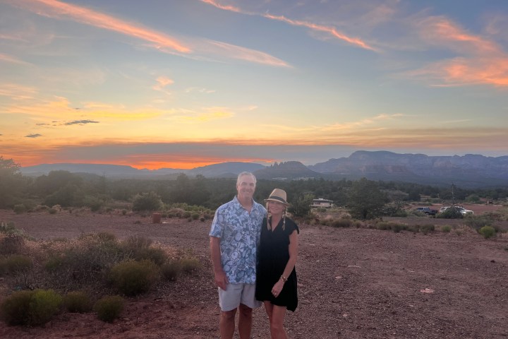 Couple posing in front of a desert landscape at sunset, with colorful sky and distant mountains.