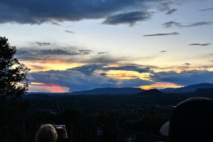 Person capturing a vibrant sunset over hilly landscape, with dramatic clouds in the sky.