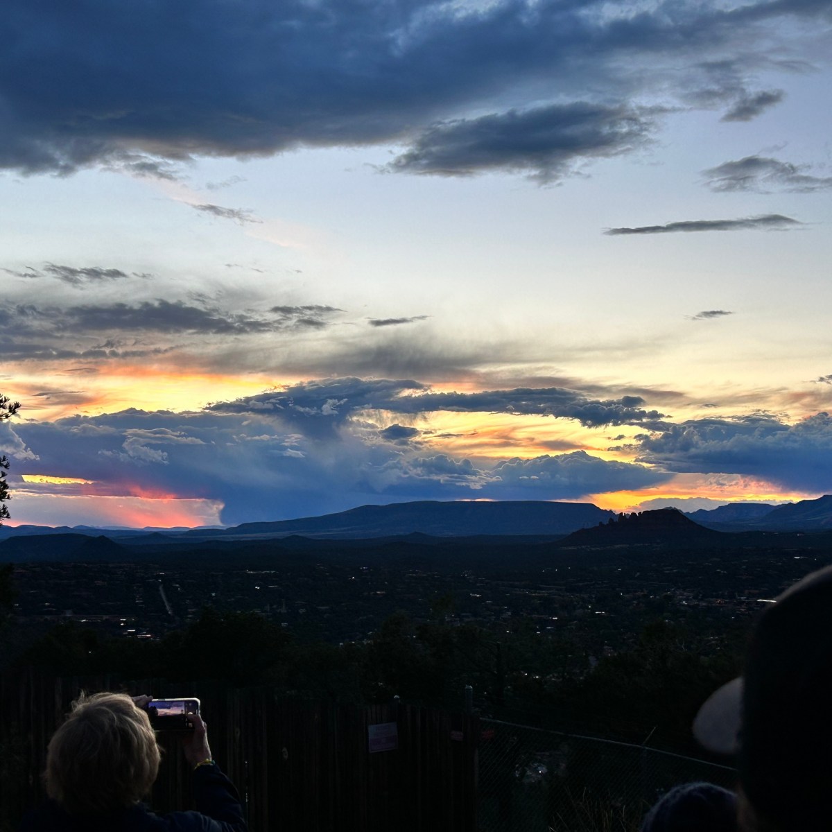 Person capturing a vibrant sunset over hilly landscape, with dramatic clouds in the sky.