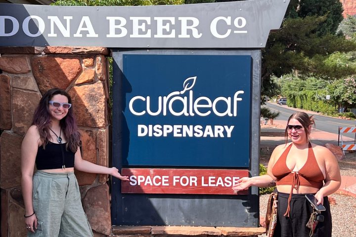 Two people pointing at a sign for Curaleaf Dispensary with 'space for lease' text beneath.