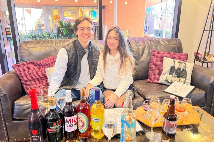 Two people seated on a sofa with assorted beverages on a table in front of them.
