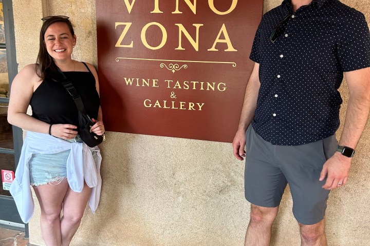 Two people smiling in front of Vino Zona wine tasting sign.