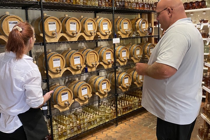 Two people standing near shelves stocked with liquor bottles and wooden barrels.