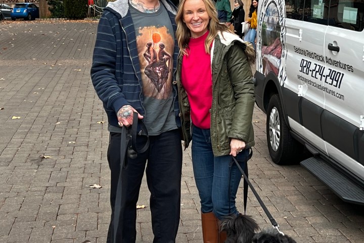 Two people with dogs posing by a van in an autumn park.