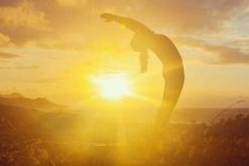 Silhouette of a person stretching with a sunrise background.