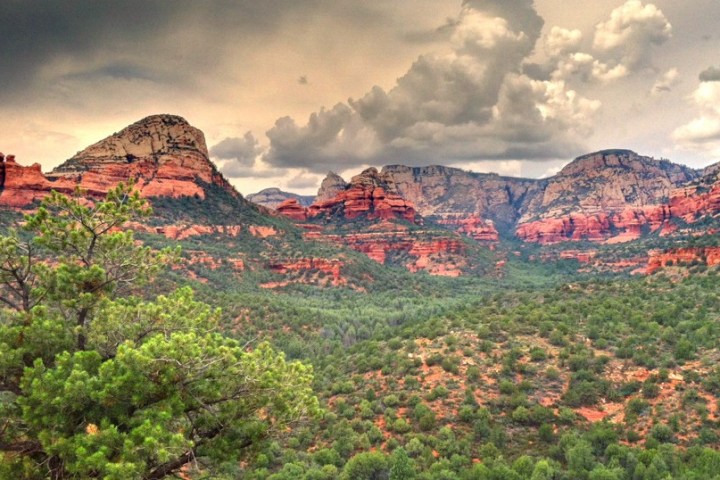 Dramatic sky over rocky red mountains and lush green forest landscape.
