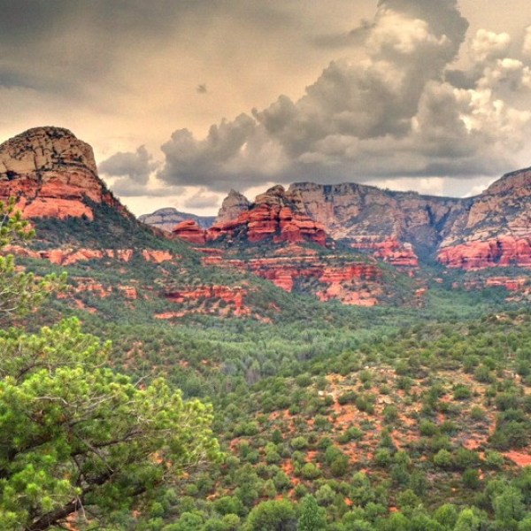 Dramatic sky over rocky red mountains and lush green forest landscape.