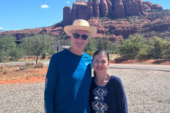 Two people posing in front of red rock formations under a clear blue sky.