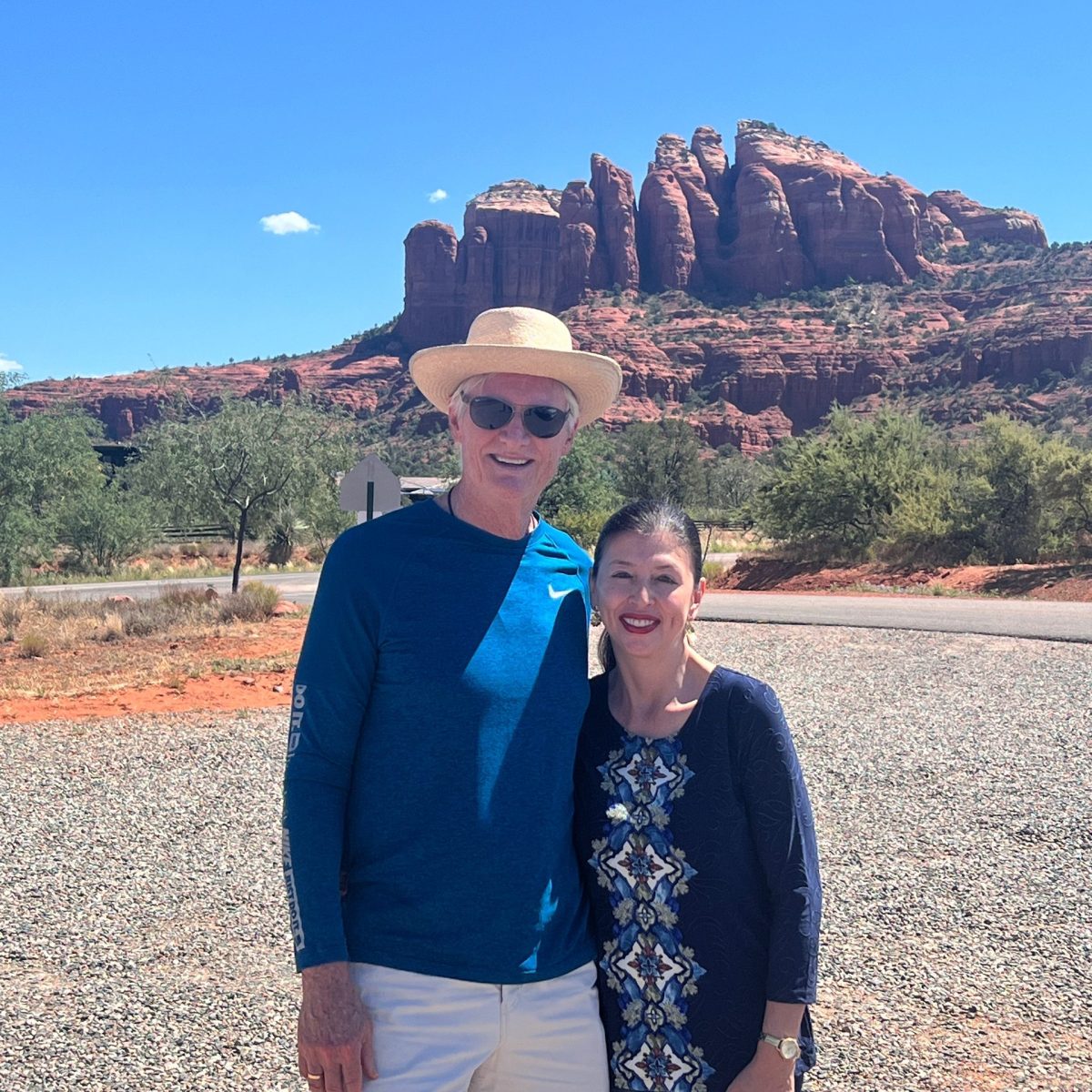 Two people posing in front of red rock formations under a clear blue sky.