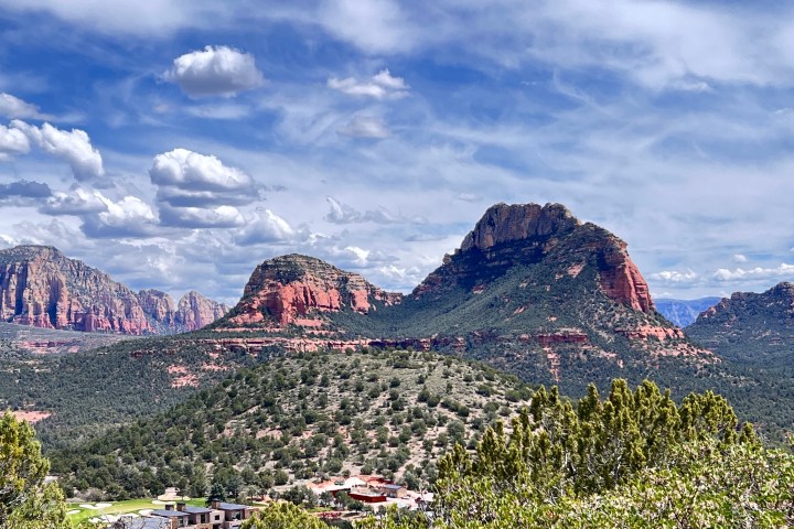 Red rock formations and green vegetation under a blue sky with clouds.
