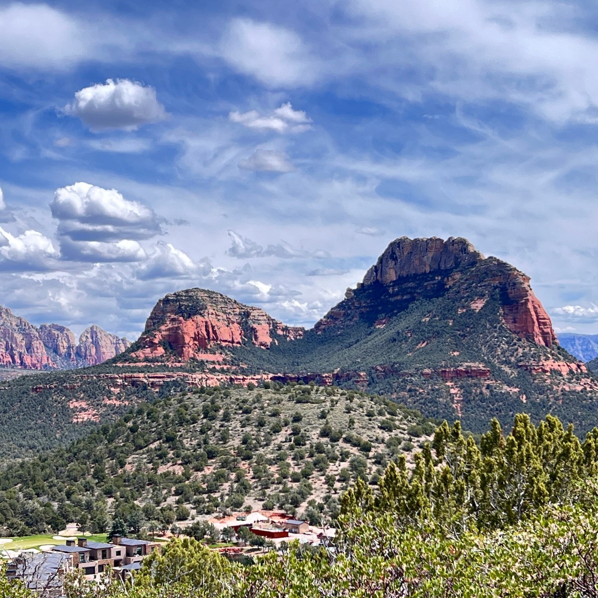 Red rock formations and green vegetation under a blue sky with clouds.