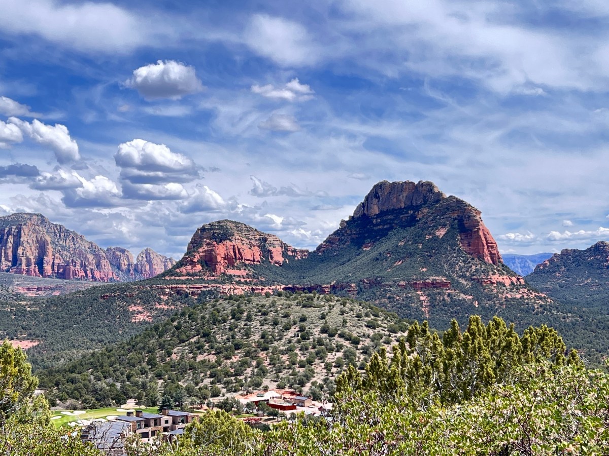 Red rock formations and green vegetation under a blue sky with clouds.