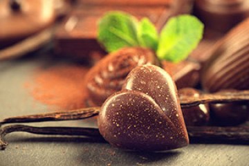 Heart-shaped chocolate piece with mint leaves and cocoa in the background.