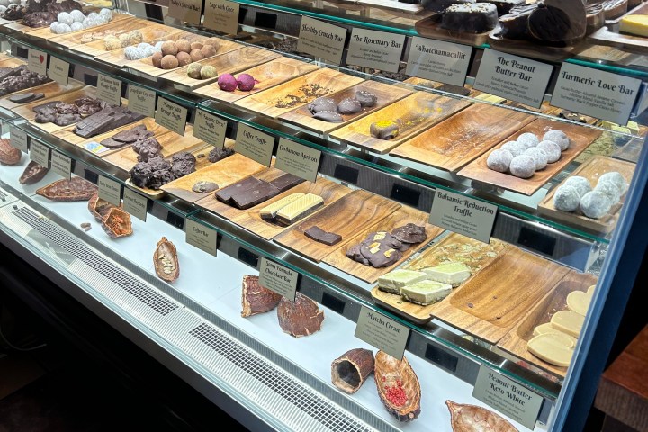 Glass display case with assorted chocolates on wooden trays in a shop.