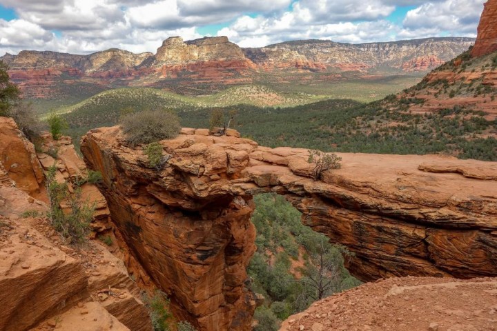 Natural stone arch bridge over a canyon with cloudy sky and distant mountains.