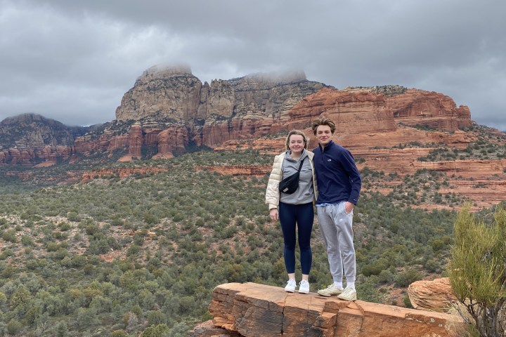 Two people posing on rock with red canyon landscape in background under cloudy sky.