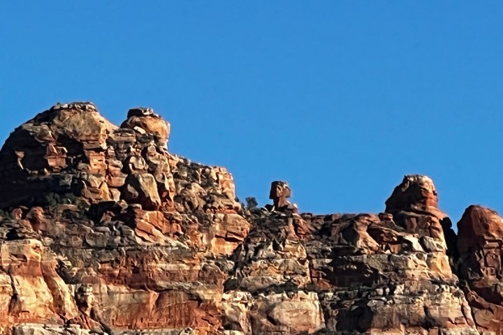 Rocky cliff with distinct formations against a clear blue sky.