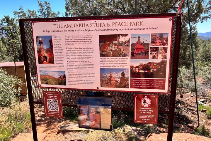 Sign for Amitabha Stupa & Peace Park with text and photos in a natural setting.