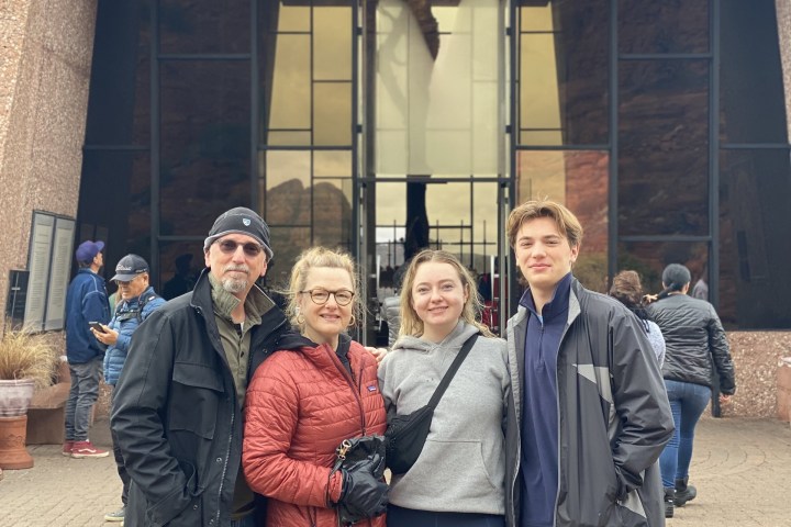 Four people posing in front of a large glass building entrance with a cross reflection.