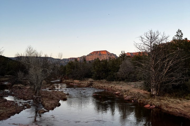 Stream flowing through rocky landscape with distant red cliffs at sunset.