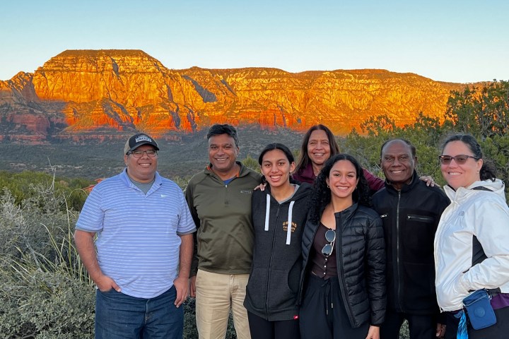 Group of seven people smiling with a sunset-lit mountain in the background.