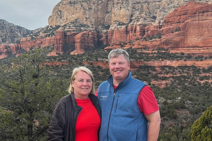 Two people standing in front of red rock mountains on a cloudy day.
