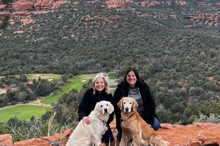 Two people with two dogs on a rocky overlook with red rock formations in the background.