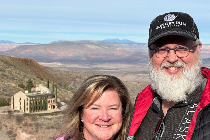 Smiling couple standing in front of a scenic landscape with hills and a distant building.