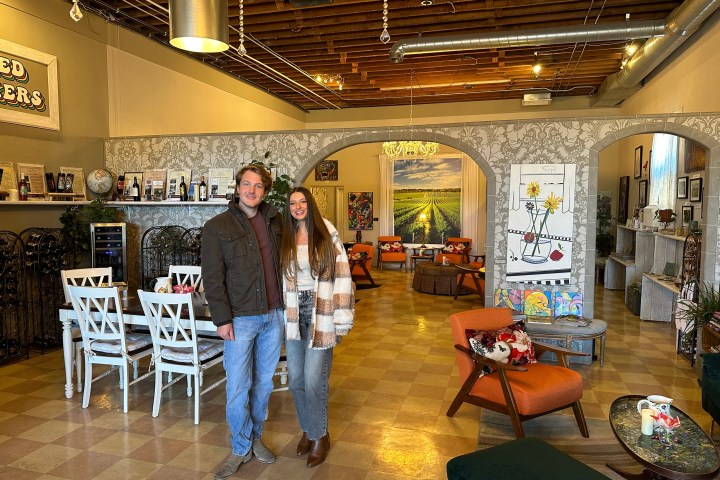 Two people in a cozy room with vintage decor and vibrant paintings on the walls.