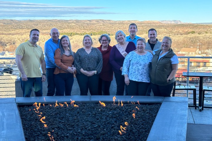 Group of 10 people posing behind a square fire pit with a scenic view in the background.