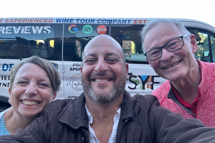 Three people smiling in front of a tour company bus.