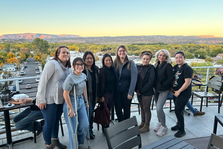 Group of eight people on a rooftop with a scenic view of mountains and trees in the background.