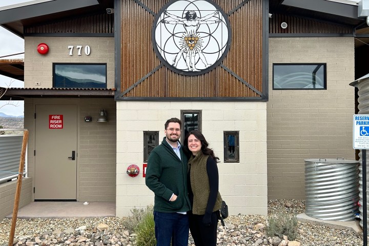 Smiling couple stands in front of a modern building with a large circular mural and number 770.