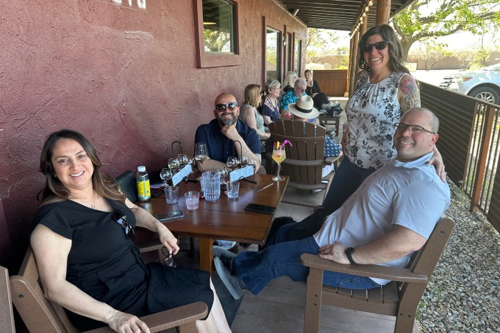 Group of people sitting and smiling on a patio with drinks on a wooden table.