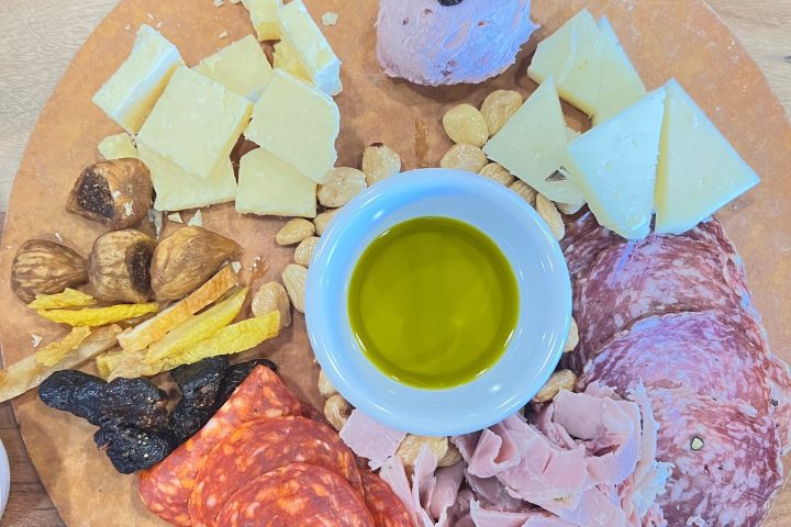 Charcuterie board with meats, cheeses, nuts, figs, yellow crisps, and a bowl of olive oil.