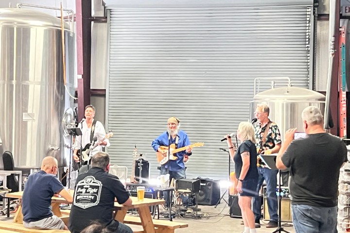 Band performing in a brewery while audience watches on benches.