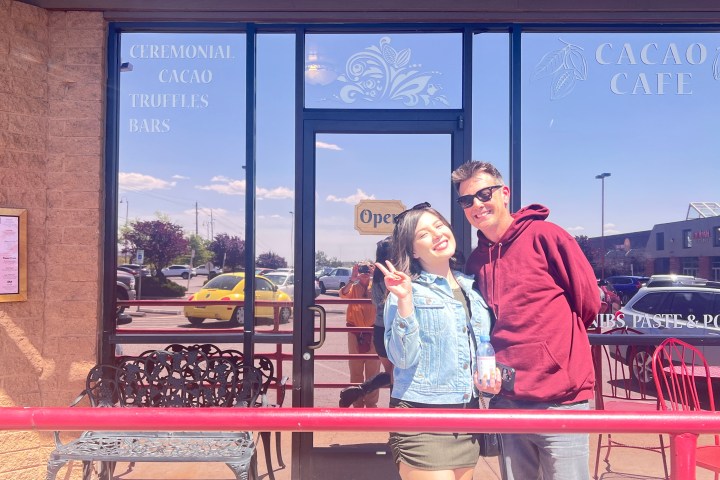 Two people smiling in front of a cacao cafe with glass doors and reflection.
