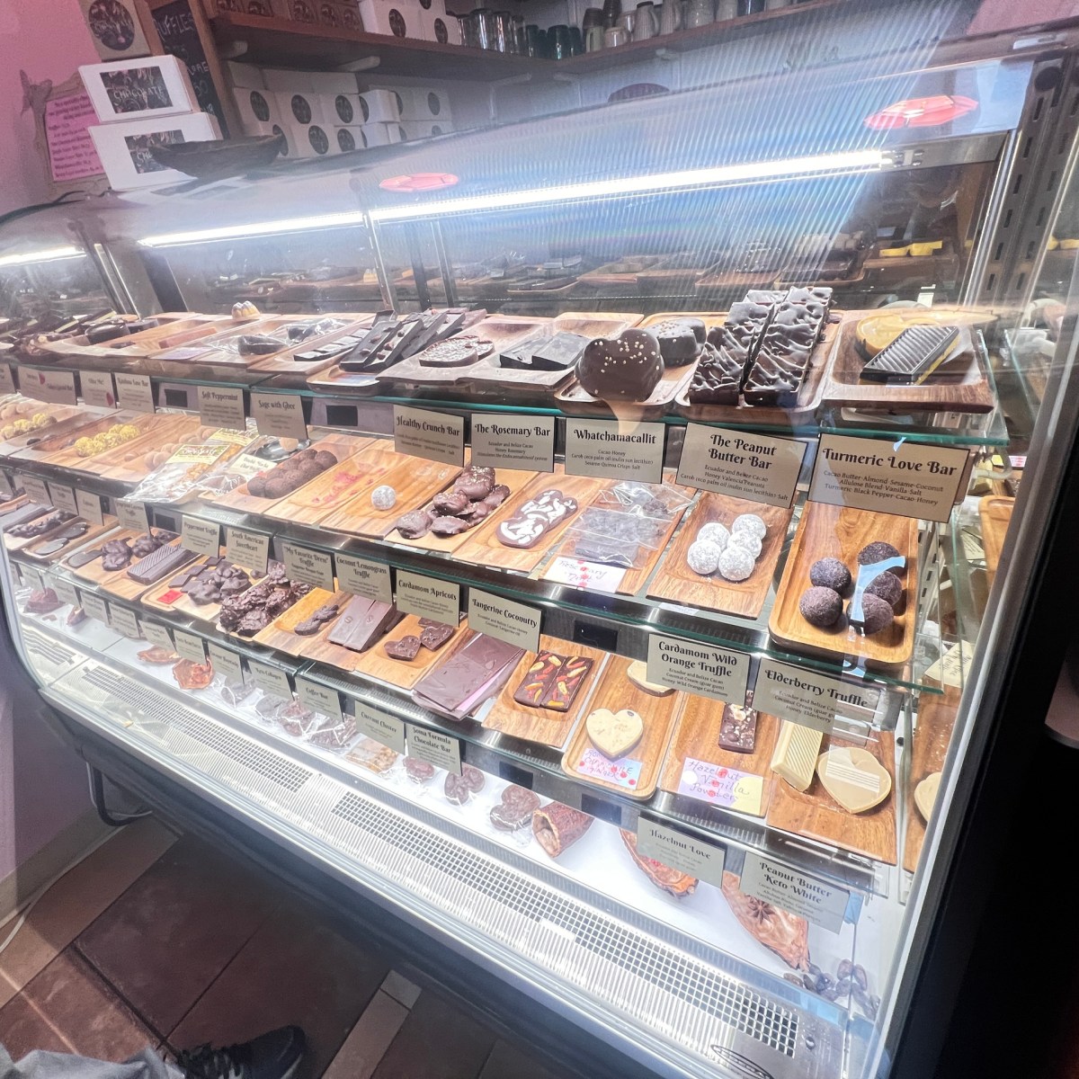 Display case with assorted chocolates and truffles on wooden trays in a shop.