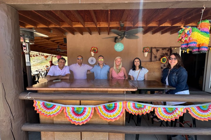 Six people sitting at a wooden table under a decorated patio.