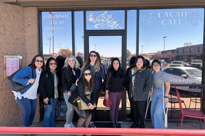 Eight people smiling in front of Cacao Cafe entrance on a sunny day.