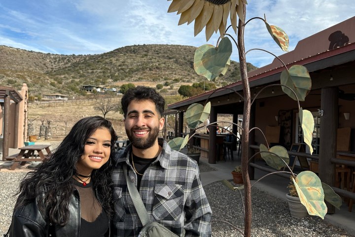 Two people standing next to a large metal sunflower sculpture outdoors.