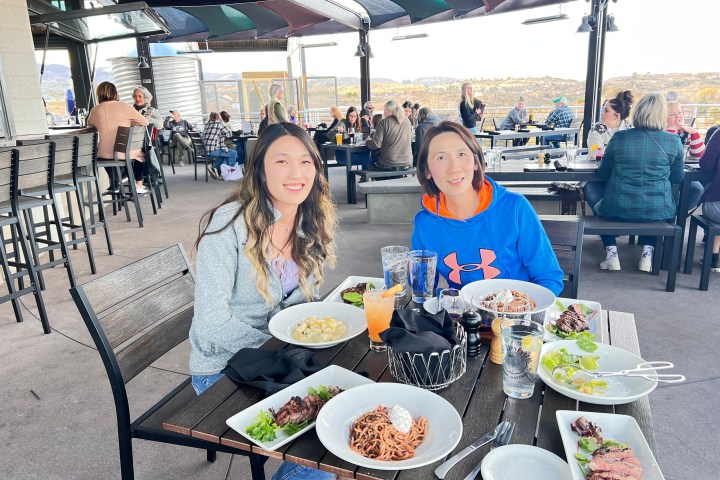Two people seated at an outdoor restaurant with plates of food and drinks on the table.