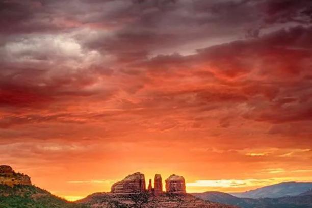 Dramatic sunset over rock formations and forest with colorful clouds in the sky.