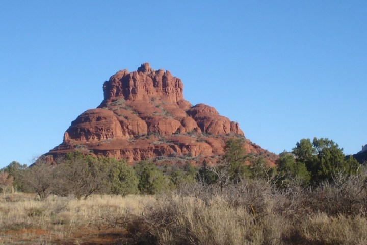 Red rock formation surrounded by trees under a clear blue sky.