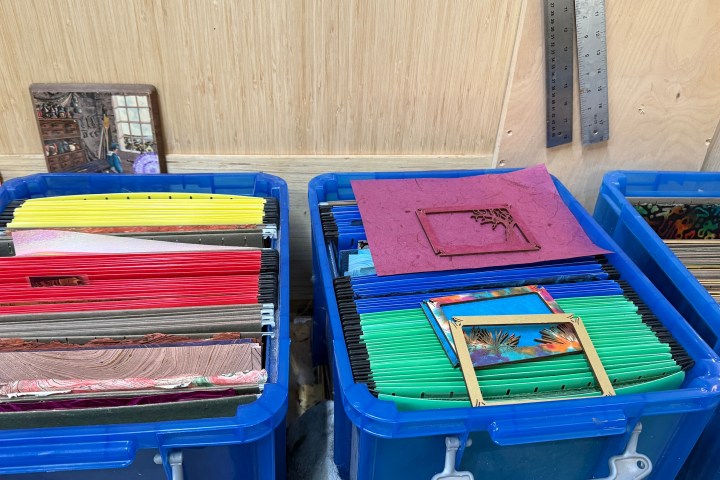 Blue bins with colorful file folders and picture frames against a wooden wall.