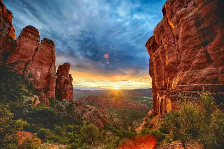 Sunset over a canyon with tall red rock formations and dramatic clouds.